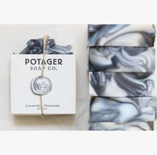 Load image into Gallery viewer, Potager Soap Co. handmade soap in the Lavender charcoal scent. Label is held onto soap with a piece of twine and a melted wax seal. The bar with a label is laying down with multiple bars nest to it showing the marbled pattern of the handmade soap.