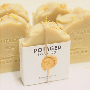 Potager Soap Co. handmade soap in the Lemongrass scent. Label is held onto soap with a piece of twine and a melted wax seal. Multiple bars without labels are in the background showing the logo engraved on to them