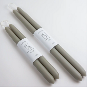 Two sets of green taper candles of differing sizes lay on white background and wrapped in white labels