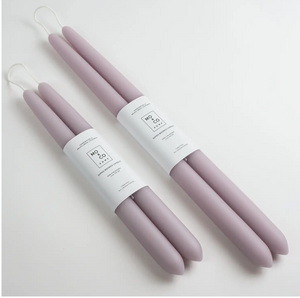 Two sets of light purple taper candles of differing sizes lay side by side on white background and wrapped in white label