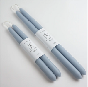 Two sets of light blue taper candles of differing sizes lay on white background and wrapped in white labels