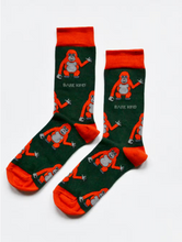 Load image into Gallery viewer, Forest green socks with deep orange cuffs, heels and toes. Deep orange orangutans with light grey faces, bellies, and hands line the socks. The name Bare Kind is written in light grey under the first row of orangutans.