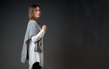 Load image into Gallery viewer, Image of woman looking at camera from the side and standing in front of dark gray background; Woman is wearing long white tunic shirt with light gray knitted shawl thrown over her shoulders