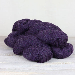 3 skeins of dark purple yarn with flecks of blue, green, and yellow throughout on white background.