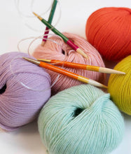 Load image into Gallery viewer, 5 colorful balls of yarn in bright orange, yellow, pink, purple, and light green/blue sit together with two sets of circular knitting needles on top on white background