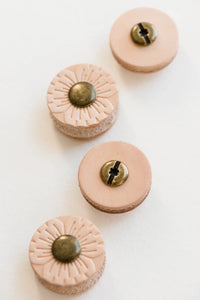 Four post buttons shown on white background with every other button flipped over to show back side; Front side of buttons show light tan flower petal-like design with round bronze colored middle; Back side of buttons show light tan with no design and round bronze colored middle piece with small hole in middle and black line running across