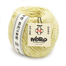 Load image into Gallery viewer, Close up of Noro Yarn in Moegi shade; Appears light yellow/green with white throughout; Shown from side with paper label wrapped around left outside edge in black and white with Japanese characters running up and down; Reads &quot;NORO&quot; &quot;the World of nature&quot; &quot;MADE IN JAPAN&quot; on tag tag attached with black tie on right side of yarn