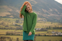 Load image into Gallery viewer, Image of redheaded woman in knitted green sweater and blue skirt against green field landscape.