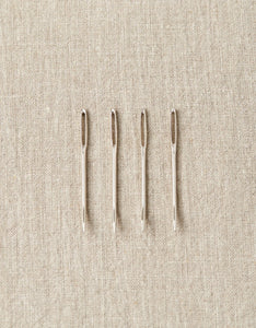 Image of four bent tip tapestry needles laid out on tan colored cloth backgound