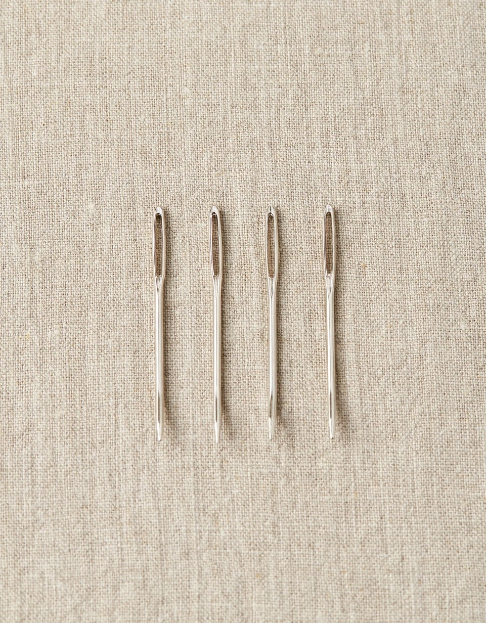 Image of four bent tip tapestry needles laid out on tan colored cloth backgound