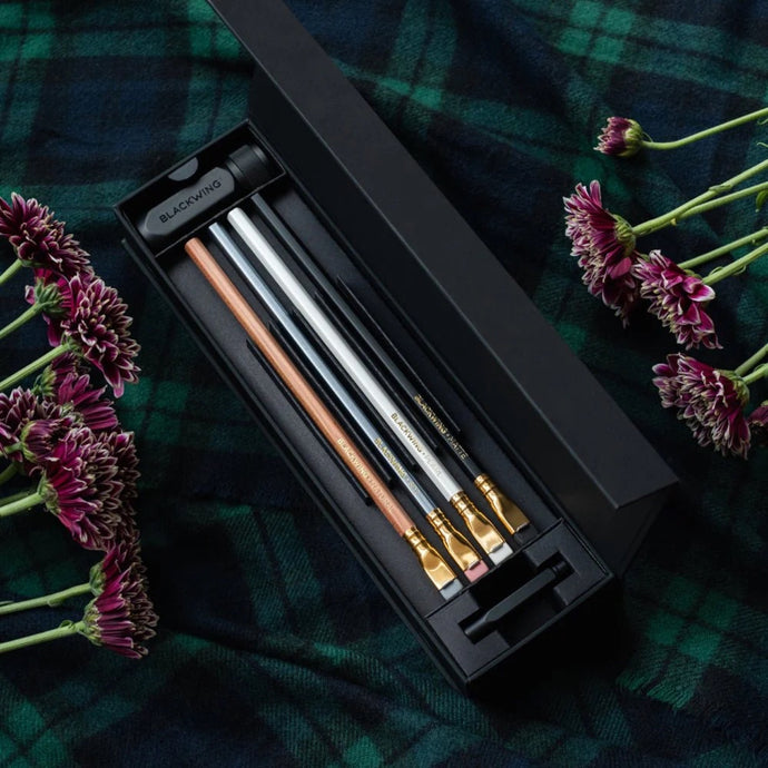 Set of Blackwing pencils in a black case on a plaid fabric background with flowers.