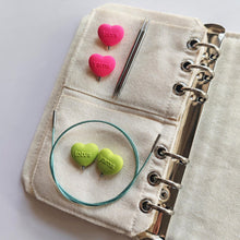 Load image into Gallery viewer, Green and Pink heart needle stoppers on a beige fabric with knitting needles and cord