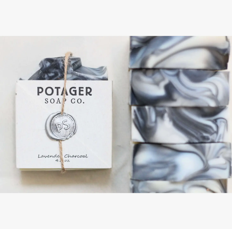 Potager Soap Co. handmade soap in the Lavender charcoal scent. Label is held onto soap with a piece of twine and a melted wax seal. The bar with a label is laying down with multiple bars nest to it showing the marbled pattern of the handmade soap.