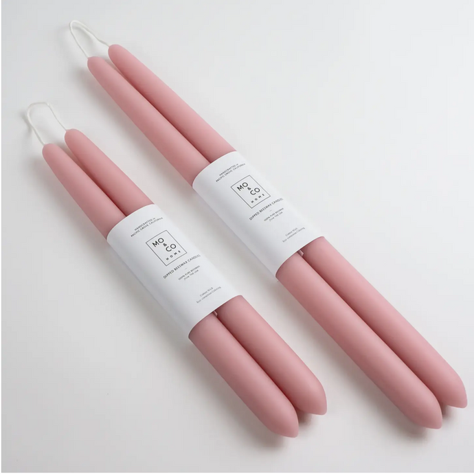 Two sets of light pink taper candles of differing sizes lay side by side on white background wrapped in white labels.