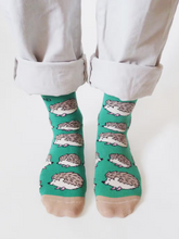 Load image into Gallery viewer, Person wearing the green and tan socks with hedgehogs, standing with white, rolled up pants. Pictured from about mid shin down.