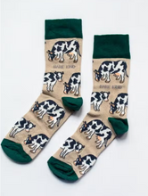 Load image into Gallery viewer, Tan socks with forest green cuffs, heels and toes. Black and white cows line the socks. The name Bare Kind is written in grey under the first row of cows. 
