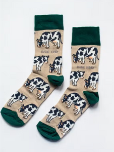 Tan socks with forest green cuffs, heels and toes. Black and white cows line the socks. The name Bare Kind is written in grey under the first row of cows. 