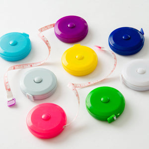 Several colorful tape measurers laid out in bright pink, dark blue, bright purple, bright green, white, light blue/gray, yellow, and bright blue on white background