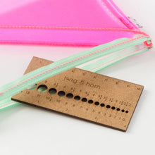 Load image into Gallery viewer, Brown needle gauge that reads &quot;twig &amp; horn&quot; half out of clear and pink zipper pouch with light green zipper