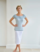 Load image into Gallery viewer, GIRL STANDING WITH HANDS ON HIPS AND LEGS CROSSED WEARING A KNIT SHORT SLEEVE BLUE TOP AND A WHITE SKIRT