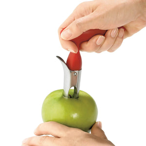 Red and stainless steel apple corer in hand of person as it goes into green apple core