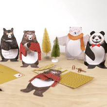 Load image into Gallery viewer, Multiple examples of bear hugs cards sit out on wooden table amidst small plastic Christmas trees. Bears wear scarves, cardigans, glasses, and bow ties. All but one bear bends at the legs and stands on own