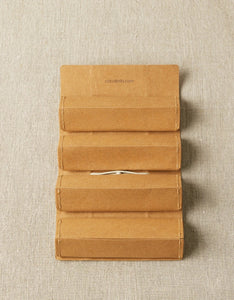 Image of unrolled accessory roll on tan background; Four compartments sectioned off in a column with white string poking through middle of second and third sections; "Cocoknits.com" text at top of roll