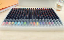 Load image into Gallery viewer, Side view of watercolor brush pens in plastic casing laying on desk. Pens displayed with black bodies and orange lettering. All colors of rainbow displayed at tips of pens with clear plastic cap covering each