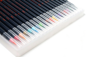 Close up of tips of watercolor brush pens in all colors of rainbow. Main body of pens shown to be black with orange lettering on the side. Tips of pens covered with small clear plastic caps