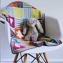 Load image into Gallery viewer, Colorful knitting blanket with many patterns laid over white chair on white background with stuffed animal gray rabbit sitting on chair with blanket