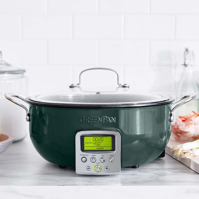 Dark green Greenpan Smart Skillet with light green screen face sitting on light gray and white kitchen countertop; Two stainless steel handles on either side, lid with stainless steel handle on top; 7 round buttons on front below screen face showing time and temperature; 