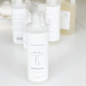 Clear plastic bottle with spray nozzle wrapped in white label that reads "Common Good, Bathroom Bergamot"