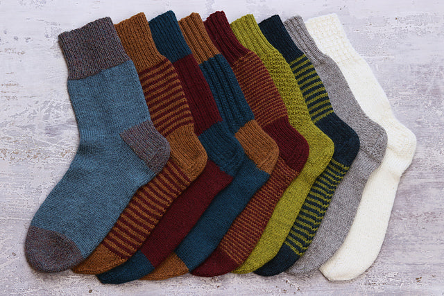 Image of several knitted socks laid out on top of each other across gray background. Socks in colors of blue, orange, red, gray, white, and green