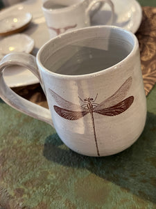 Off white mug with image of brown dragonfly on front sitting on green metal table