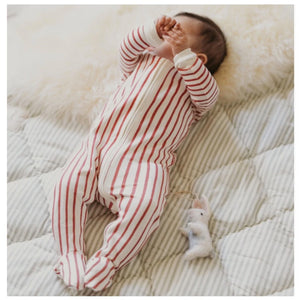 Baby in red and white striped sleeper lays on white background next to ornament of a white bunny