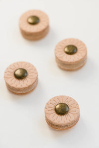 Image of four post buttons in zig zag pattern on white background with front button in focus and following buttons more and more blurred; Buttons are light tan in color with bronze colored middle section and flower-like line indentions spraying out from bronze middle