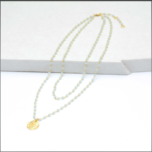 Image of yellow gold-plated necklace on white background. Necklace broken up by light blue beads throughout and medallion drop pendant in middle.