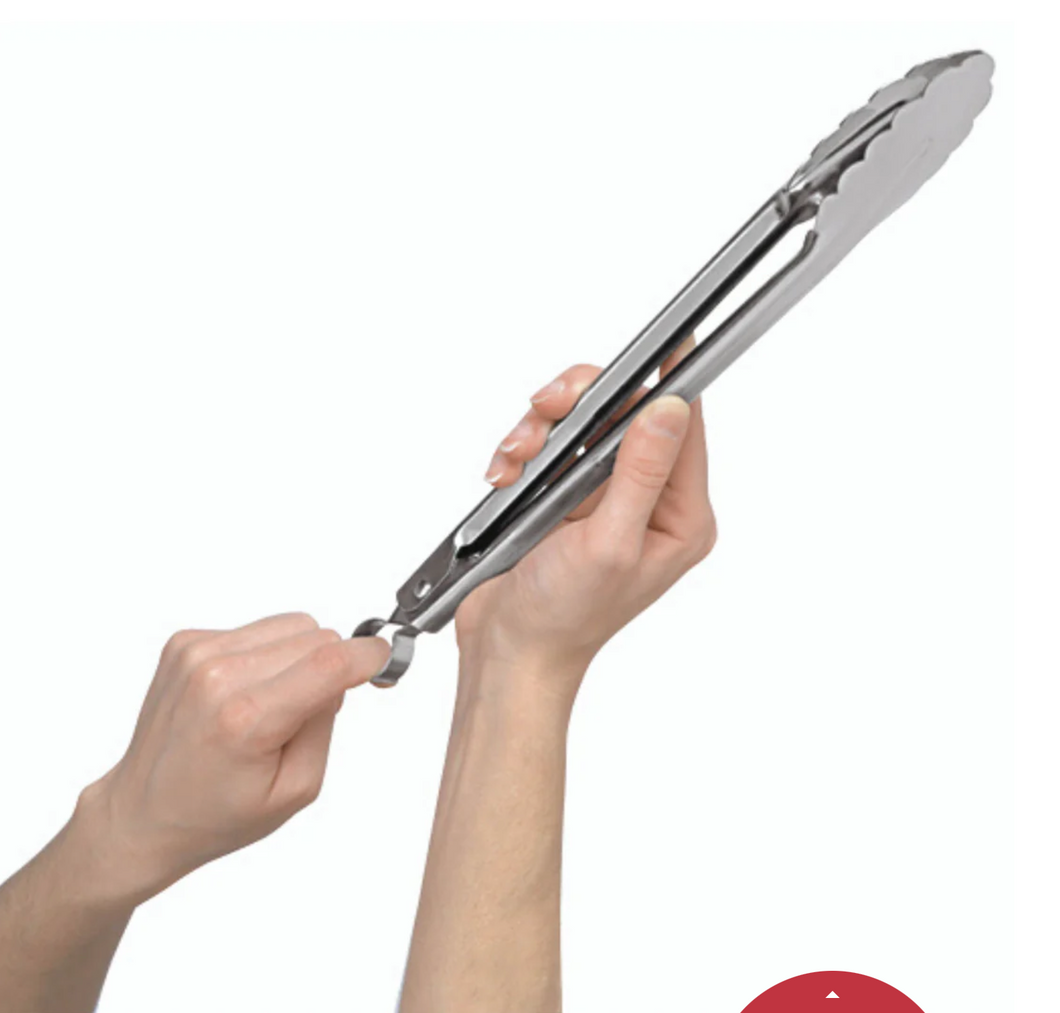 Stainless steel locking tongs pictured in woman's hands on white background; Right hand holds middle of tongs while left hand is pulling locking mechanism loop at bottom of tongs; Top of tongs have scalloped edges in top right corner of image