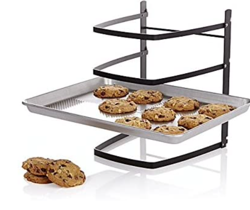  A black four tiered cooling rack supports a gray baking sheet on the third level down. The baking sheet holds several cookies on it