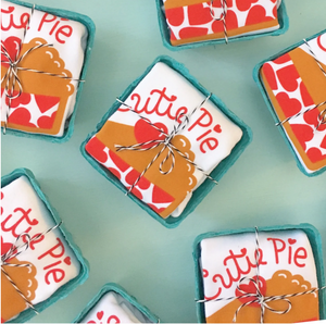 Egg cartons with white onesie that read "Cutie pie" in red with image of pie below are laid out on green background and tied up with string