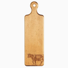 Load image into Gallery viewer, Image of long wooden cutting board on white background. Image of a cow has been burned into bottom right corner while top features rounded handle with hole in middle