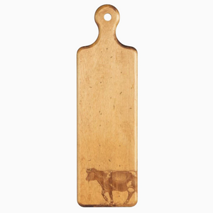 Image of long wooden cutting board on white background. Image of a cow has been burned into bottom right corner while top features rounded handle with hole in middle