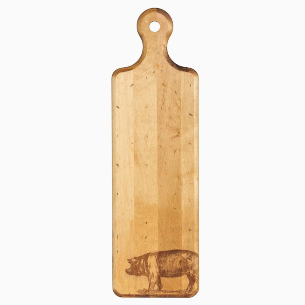 Image of long wooden cutting board on white background. Image of a pig has been burned into bottom right corner while top features rounded handle with hole in middle