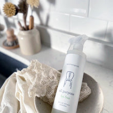 Load image into Gallery viewer, Image of Common Good All Purpose Tea Tree spray bottle resting in small bowl with dish rag on white kitchen counter top with white backsplash behind and wooden bottle brushes in far corner 