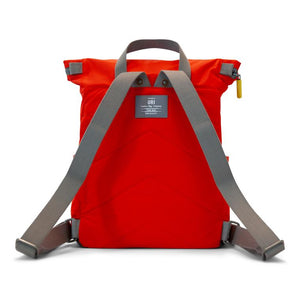 Back of red ORI backpack with gray straps and yellow zipper on white background