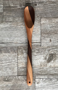 Wooden spoon with three variations of color running up in stripes. Dark, light, and medium brown wood stripes make up spoon on light gray background