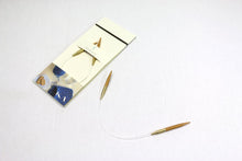 Load image into Gallery viewer, Circular knitting needles laid out in packaging and next to packaging on white background; Tips of needles are light brown in color with gold colored caps and clear connectors between; Packaging is light tan with &quot;SEEKNIT&quot; written in middle in front of needles; Thin black band at top of packaging and image of blue yarn, small glass of water, small white plate with two rectangular cookies, and part of blue knitted project depicted on bottom of packaging