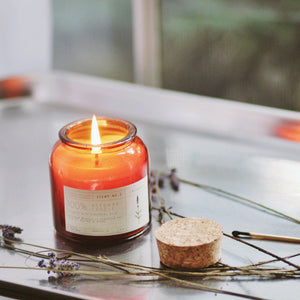 Lavender scented candle. Red/orange glass bottle with a cork top, white label with black lettering.