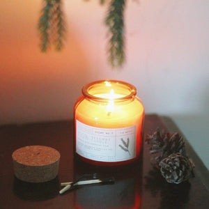 Fir needle scented candle. Red/orange glass bottle with a cork top, white label with black lettering.